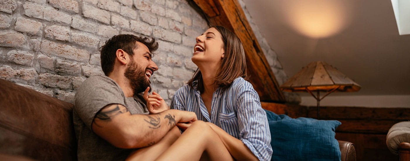 Una coppia si abbraccia e scherza su un divano all'interno della propria casa